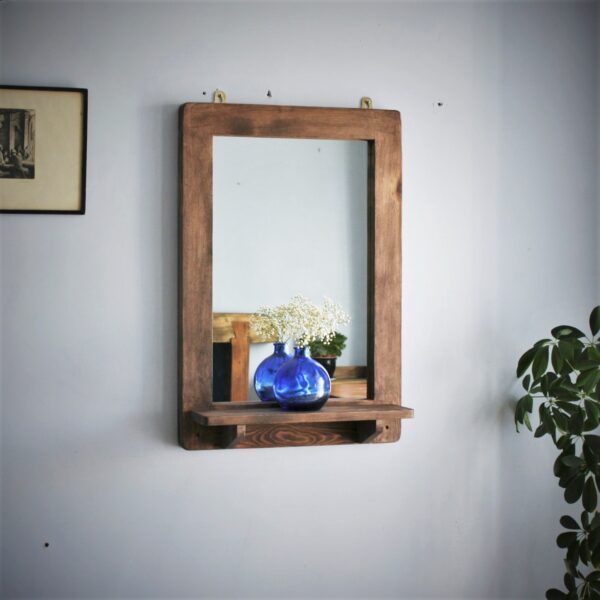 Wooden mirror with shelf in portrait with blue glass ornament and white flowers.