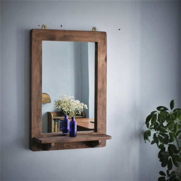 Wooden mirror with shelf in portrait with blue glass vase.