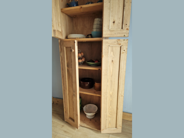 Tall kitchen larder pantry cabinet in natural wood with 2 sets of doors wide open, close up of lower shelves.