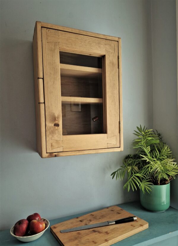 Glass door kitchen cabinet in rustic natural wood. Curio display glazed kitchen wall cabinet, low view. Handmade in Somerset UK.