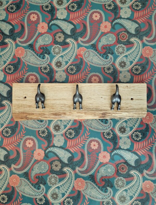 Live edge coat rack with 3 ‘waggy dog tails’ cast iron hooks on a chunky natural Oak plaque, paisley wallpaper.